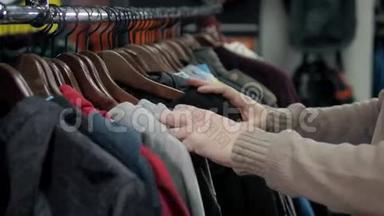 在一家零售服装店，男士毛衣和不同颜色的衬衫挂在衣架上，男士则选择店里贴身的帽衫